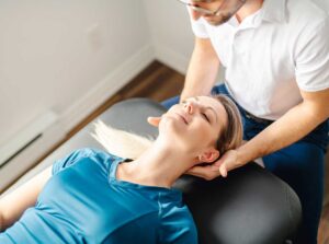 Person sitting on an exam table with a clinician gently checking their neck and upper back.