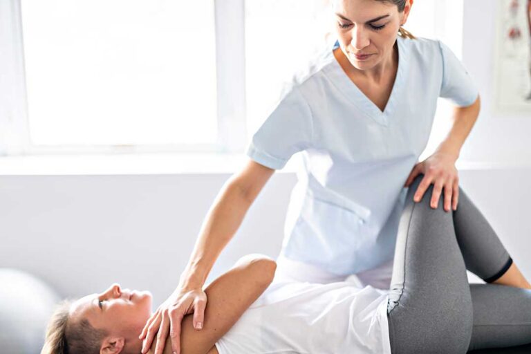 A chiropractor explaining a spine model to a patient in a well-lit clinic exam room.