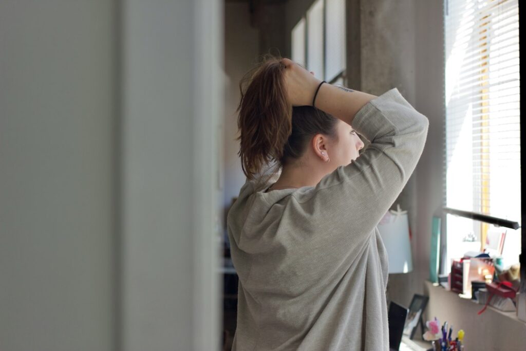Person practicing a gentle lower-back stretch beside a chair in a quiet home setting.