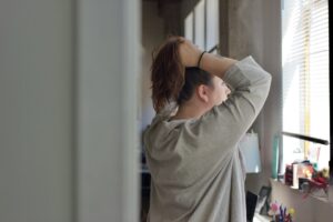 Person practicing a gentle lower-back stretch beside a chair in a quiet home setting.